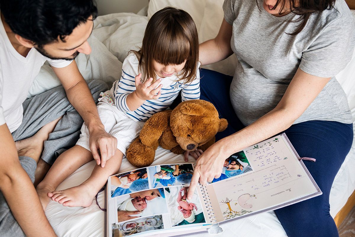 Père, mère enceinte et leur petite fille regardent un album photo
