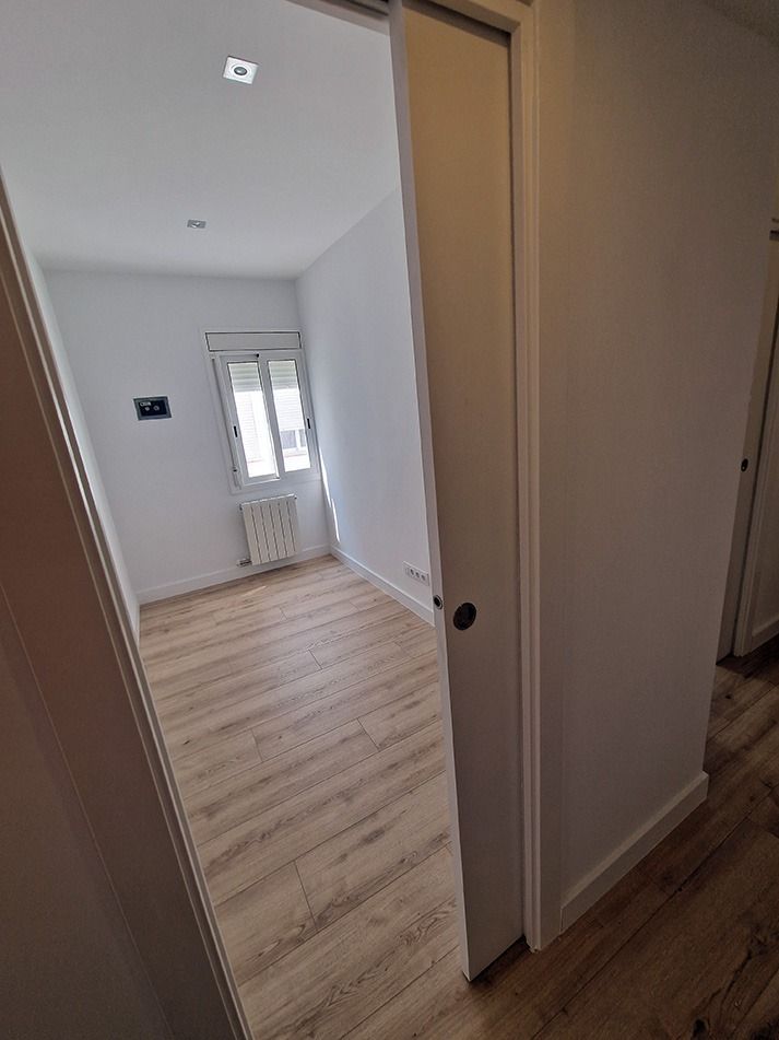 Un pasillo con una puerta corrediza que conduce a un dormitorio con pisos de madera.