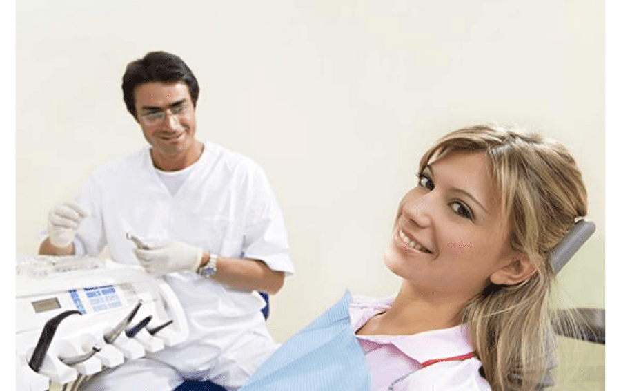 Una mujer está sentada en una silla dental con un dentista detrás de ella.