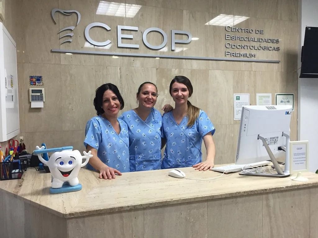 Tres mujeres con uniformes azules posan para una fotografía en un consultorio dental.