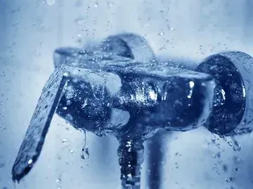 Wasser strömt aus einem verchromten Duschhahn, Tropfen glitzern vor blauem Hintergrund.