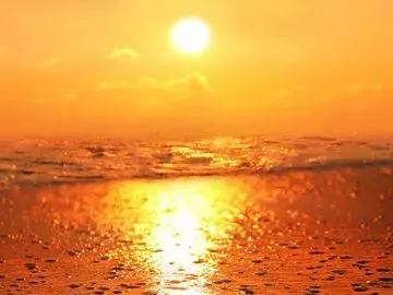 Sonnenuntergang über dem Meer, der Wasser und Sand in orangefarbenes Licht taucht.