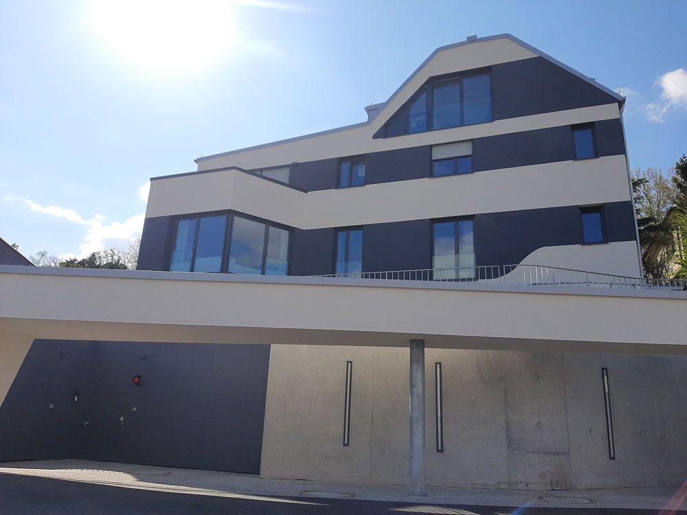 Modernes Mehrfamilienhaus mit Garage, abwechselnd graue und beige horizontale Streifen, sonniger Tag.