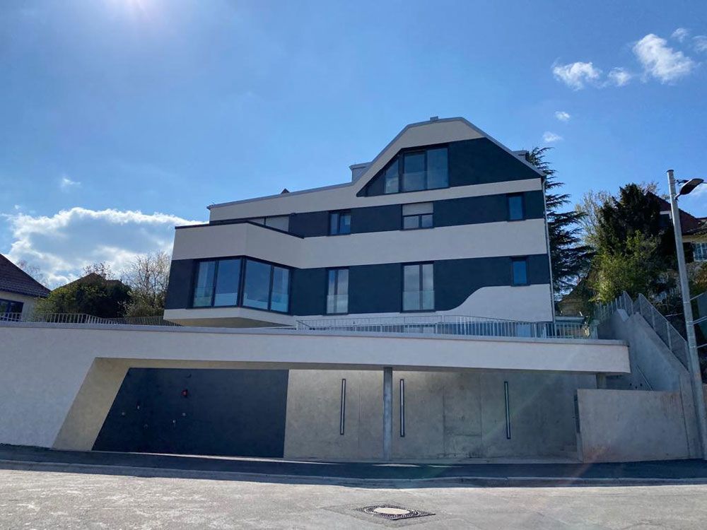 Modernes mehrstöckiges Gebäude mit überdachtem Parkplatz unter strahlend blauem Himmel.