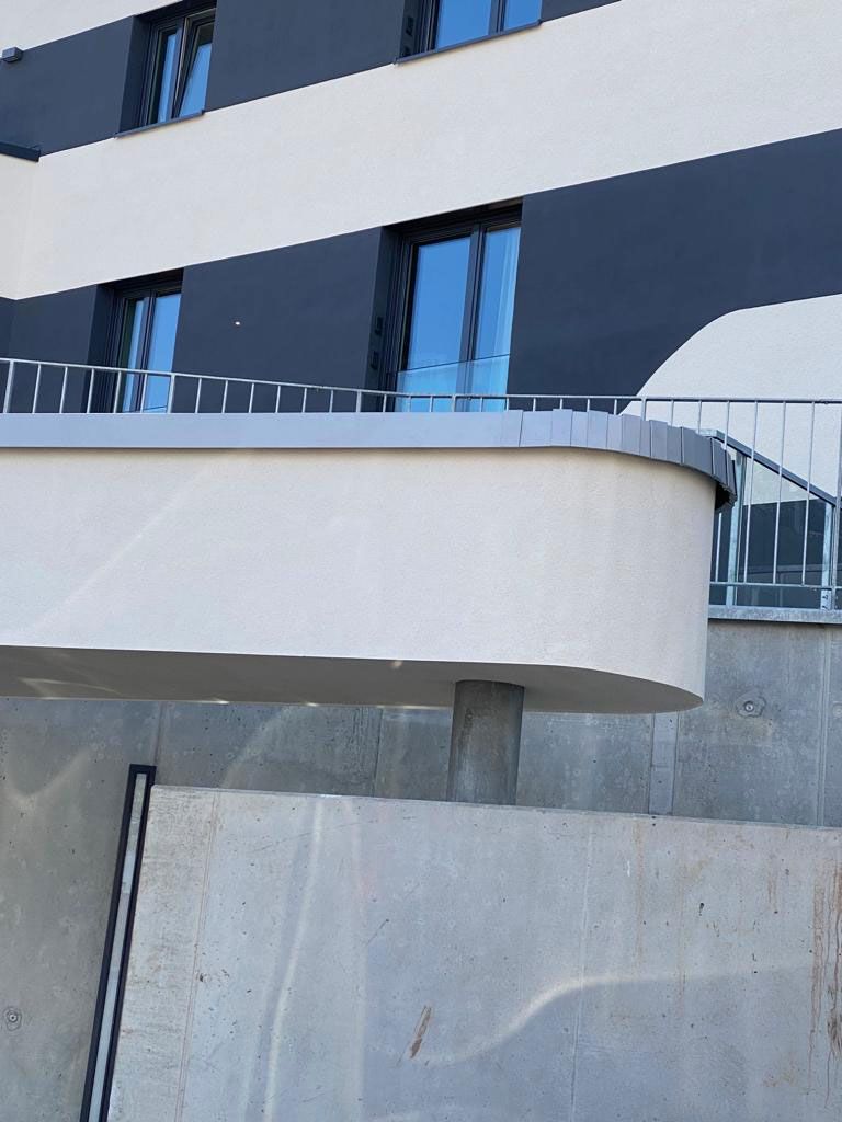 Modernes Gebäude mit einem geschwungenen, von einer Säule getragenen Balkon und dunklen und hellen Wandpaneelen.