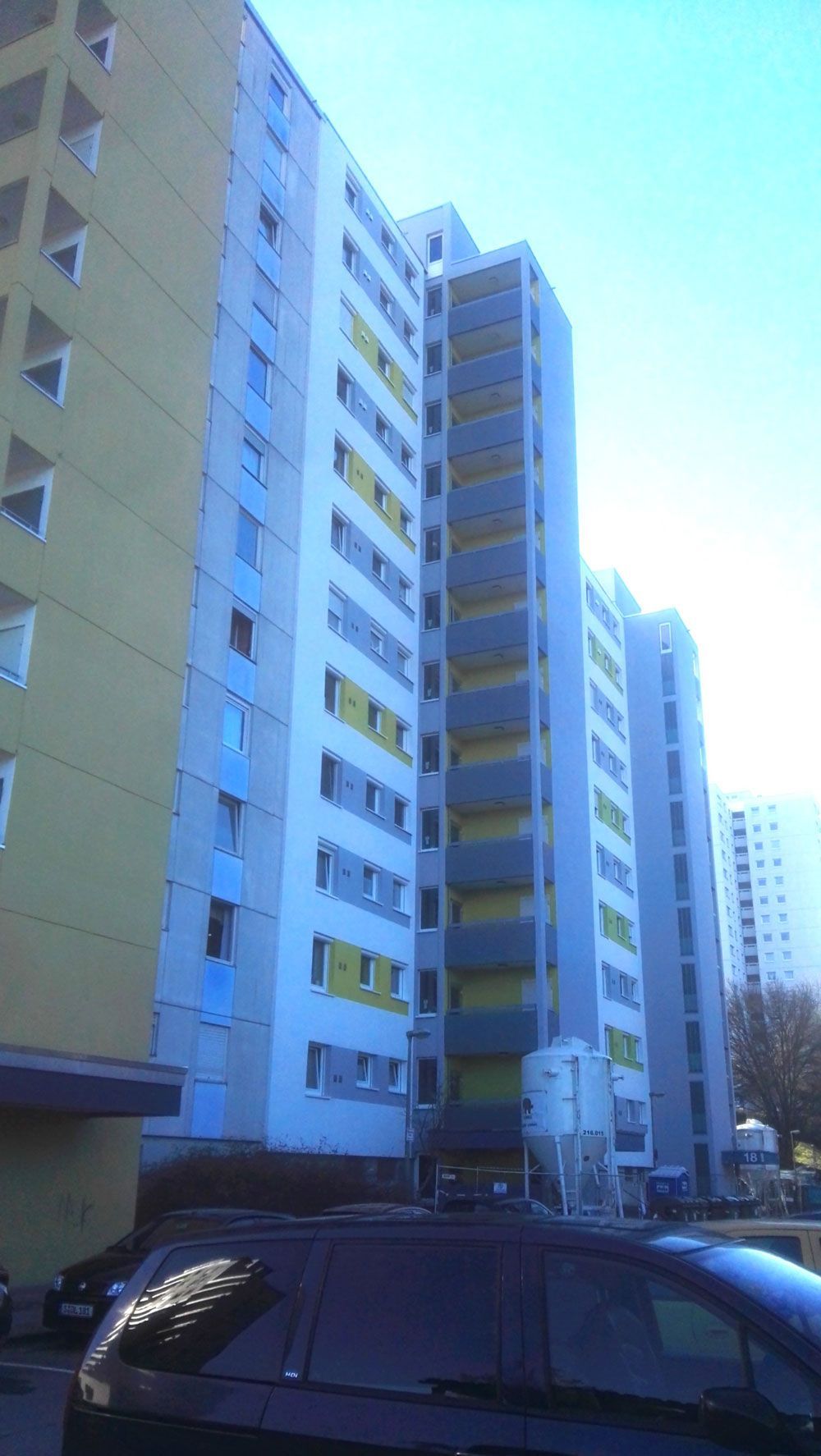 Hohe Wohnhäuser mit gelben und blauen Akzenten, von der Straße aus gesehen.