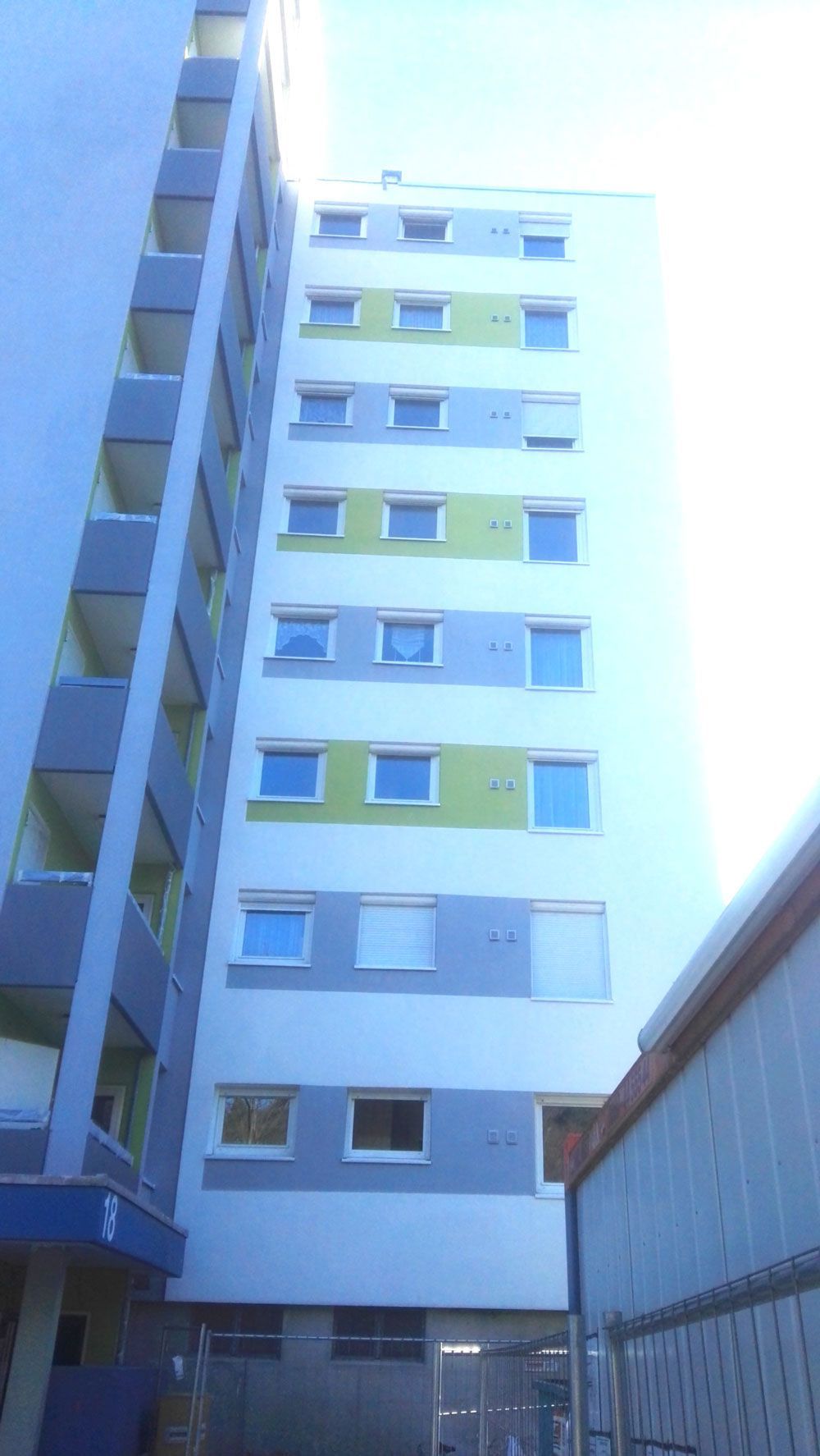 Hohes Wohnhaus mit Balkonen, graue, blaue und grüne Fassade.