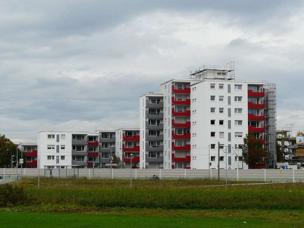 Weiße Wohnhäuser mit roten Balkonen vor bewölktem Himmel.
