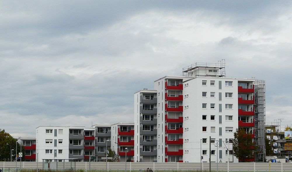 Weiße Wohnhäuser mit roten Balkonen unter bewölktem Himmel.
