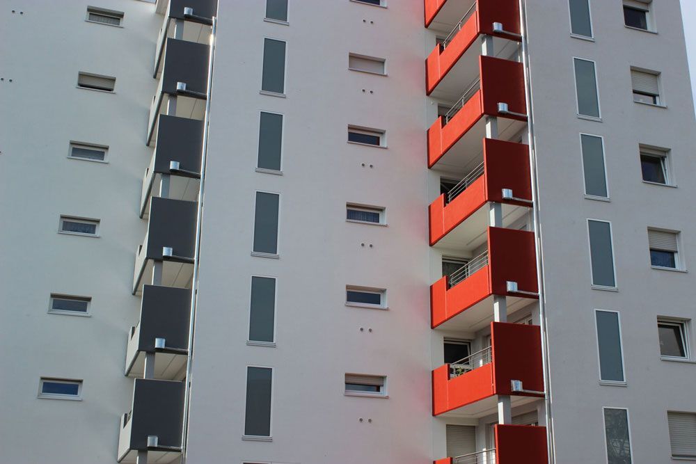 Hochhaus-Wohngebäude mit weißer Fassade, weißen Fenstern und rot-schwarzen Balkonen.