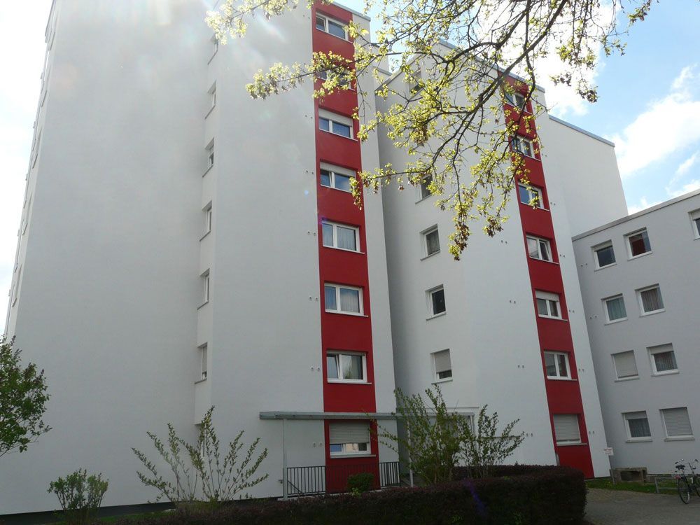 Hohes, weißes Wohnhaus mit roten Akzenten, Fenstern und Grünanlagen.