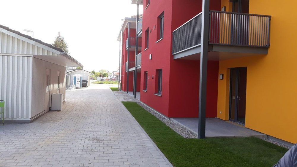 Gebäude mit roten und gelben Wänden, ein gepflasterter Weg und eine kleine Rasenfläche.