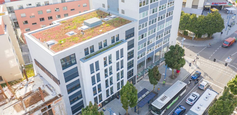 Luftaufnahme eines modernen Gebäudes mit Gründach, Stadtbussen und einer Kreuzung.