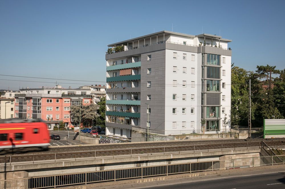 Luftaufnahme eines weißen Geschäftsgebäudes mit grauem Dach und Bäumen vor einer Bergkulisse.