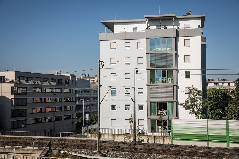Moderne Wohnhäuser neben Bahngleisen vor strahlend blauem Himmel.