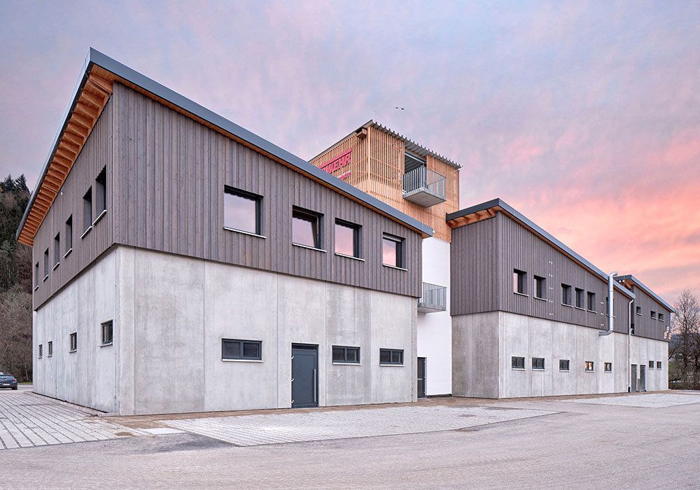 Modernes Gebäude mit Betonfundament, Holzverkleidung und schrägem Dach vor dem Abendhimmel.