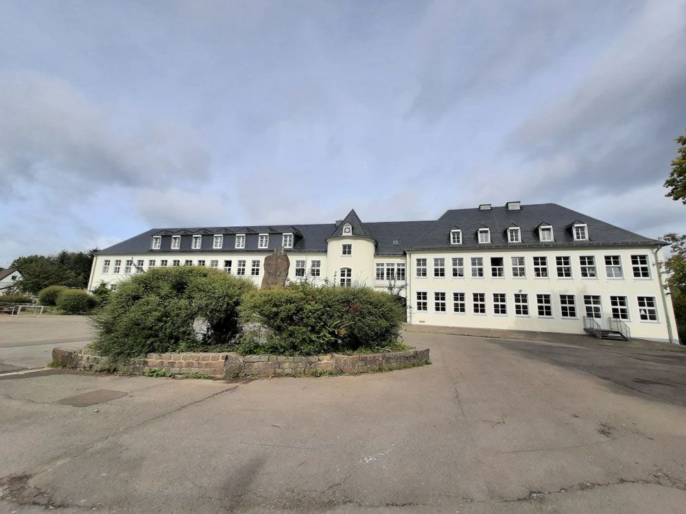 Großes, weißes Gebäude mit vielen Fenstern unter einem bewölkten Himmel.