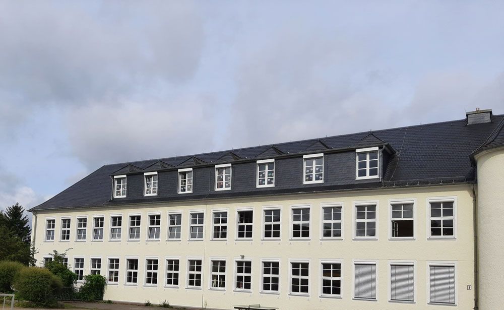 Zweistöckiges Gebäude mit vielen Fenstern, dunklem Dach, unter bewölktem Himmel.