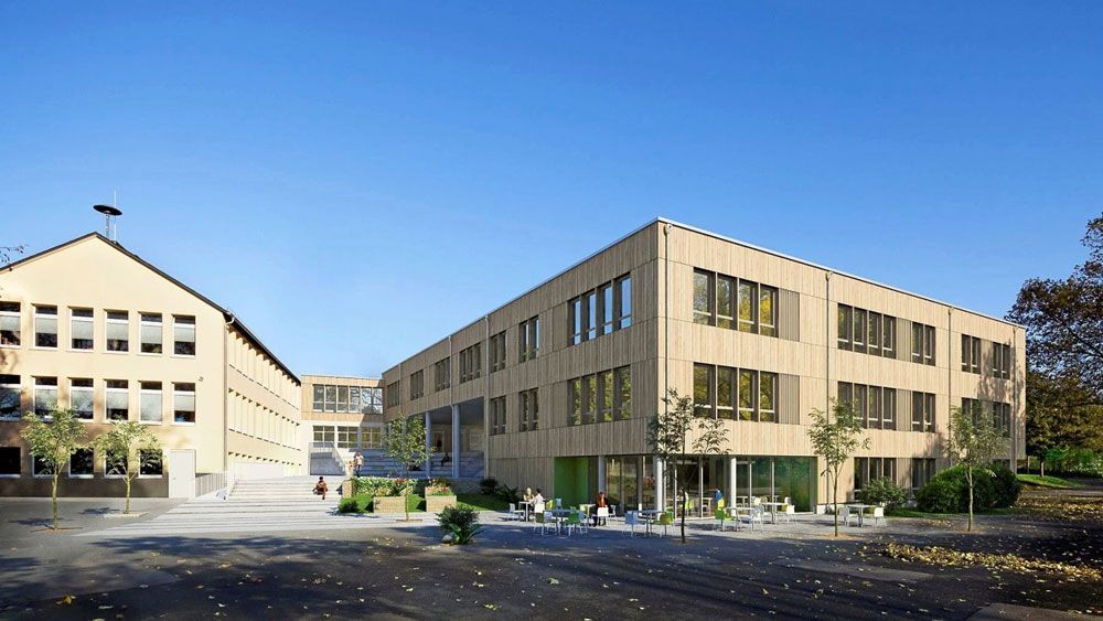 Moderne Schulgebäude mit heller Holzverkleidung und großen Fenstern, blauer Himmel.