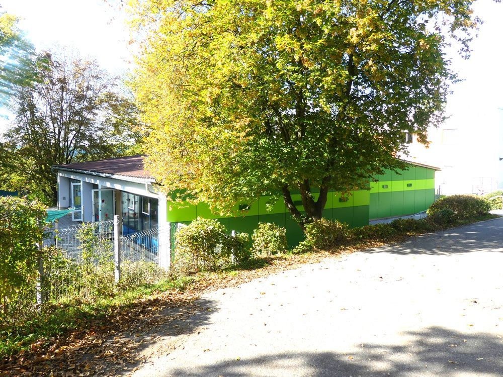 Grünes Gebäude mit Bäumen davor, eine gewundene Straße und ein bewölkter Himmel.