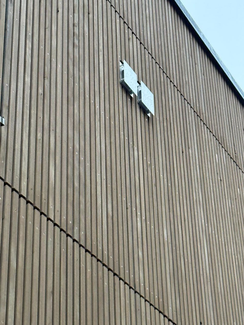 Braune Holzfassade mit zwei silbernen Metallquadraten.