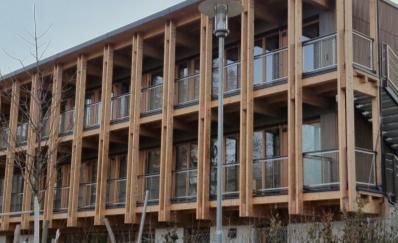 Zweistöckiges Holzgebäude mit Balkonen, sichtbaren Holzbalken und einem Lichtmast.