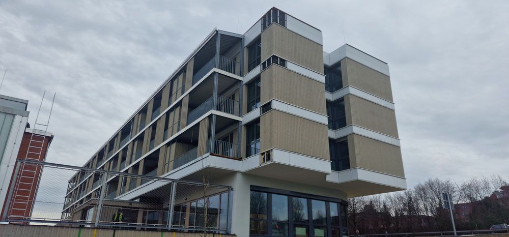 Modernes mehrstöckiges Gebäude mit Balkonen, Glasfenstern und bewölktem Himmel.