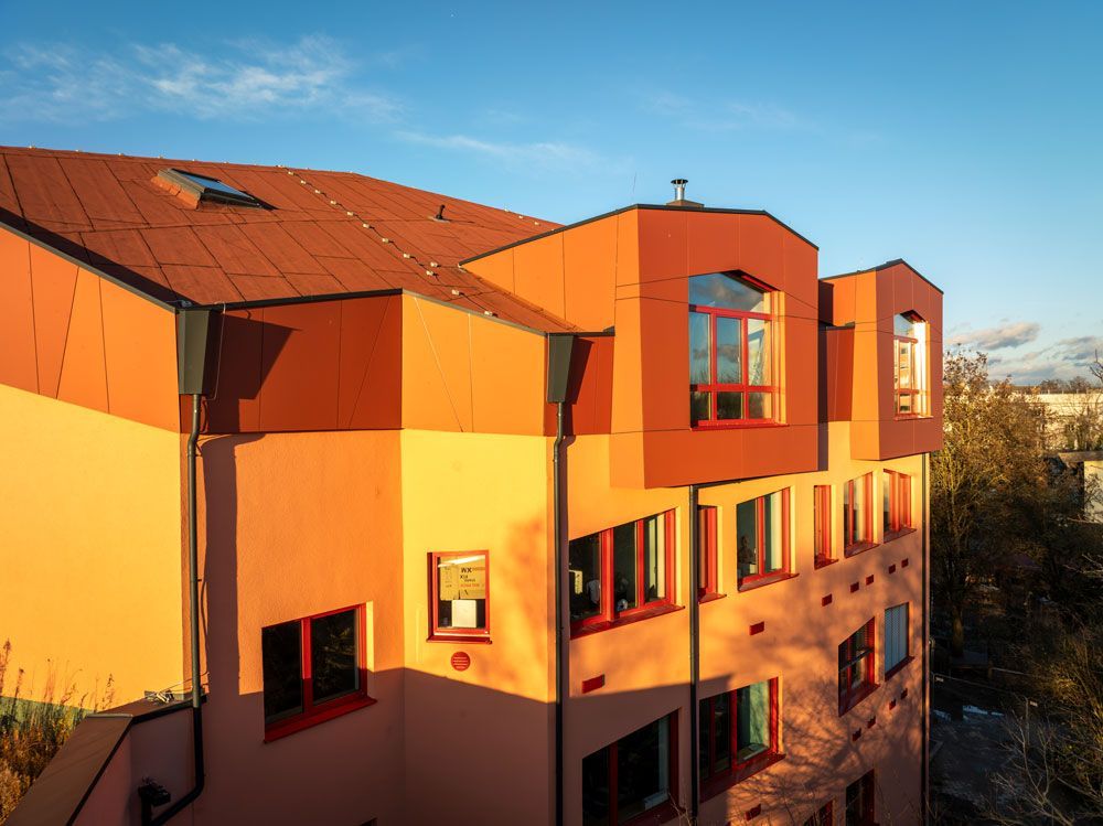 Ein orange-pfirsichfarbenes Gebäude mit schrägem Dach vor blauem Himmel.