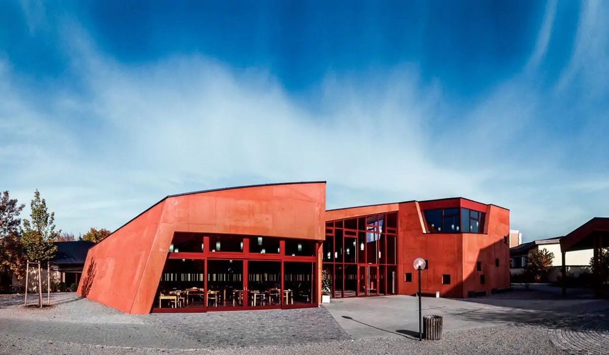 Ein rotes, kantiges Gebäude unter blauem Himmel, vermutlich ein öffentlicher Platz.