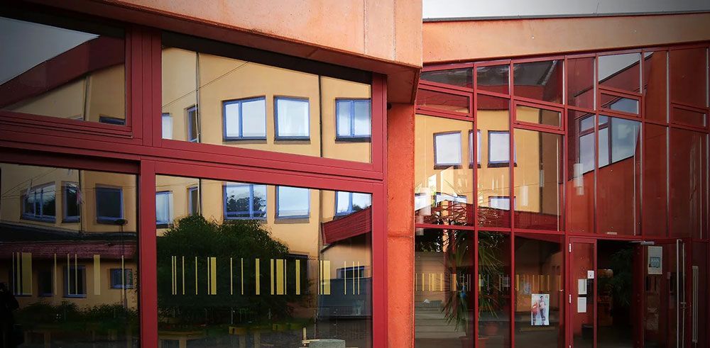 Außenansicht eines modernen Gebäudes mit rotem Rahmen und Glaswänden, das die Umgebung widerspiegelt.