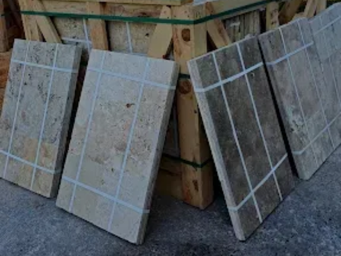 Plusieurs carreaux de pierre rectangulaires aux tons brun clair, appuyés contre une caisse en bois.