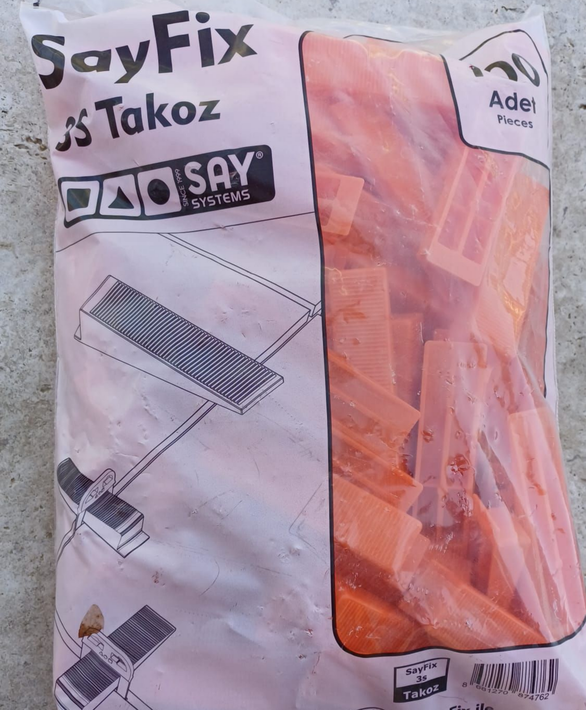 Pose de grands carreaux blancs à motif marbre sur un sol en béton, avec des cales de nivellement.