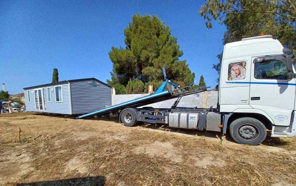 Un camión blanco está remolcando una casa móvil en un campo.