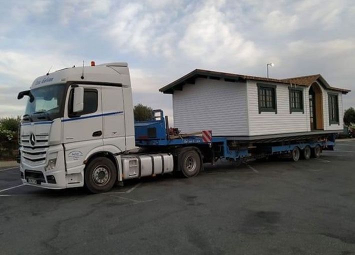 Un camión blanco transporta una casa pequeña en un remolque.
