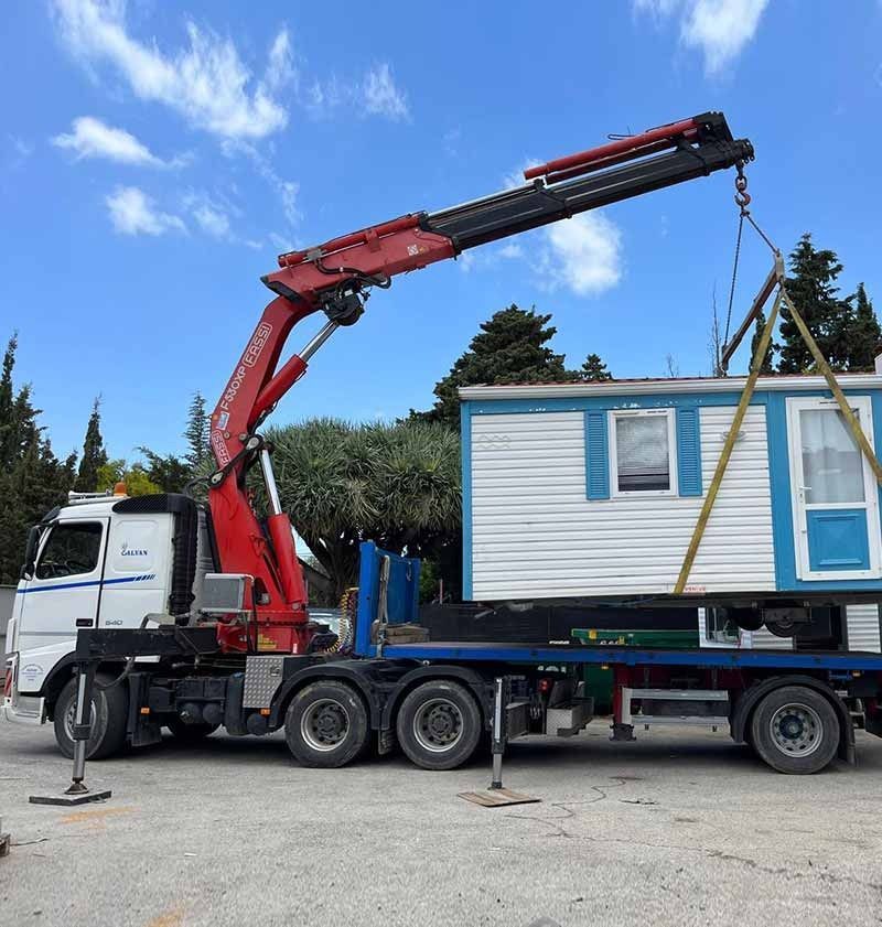 Un camión con una grúa acoplada transporta una casa.
