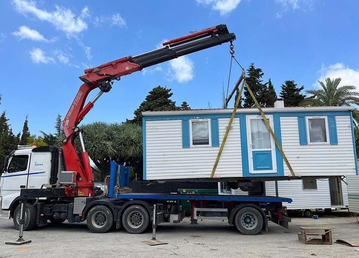 Un camión con una grúa acoplada transporta una casa móvil.