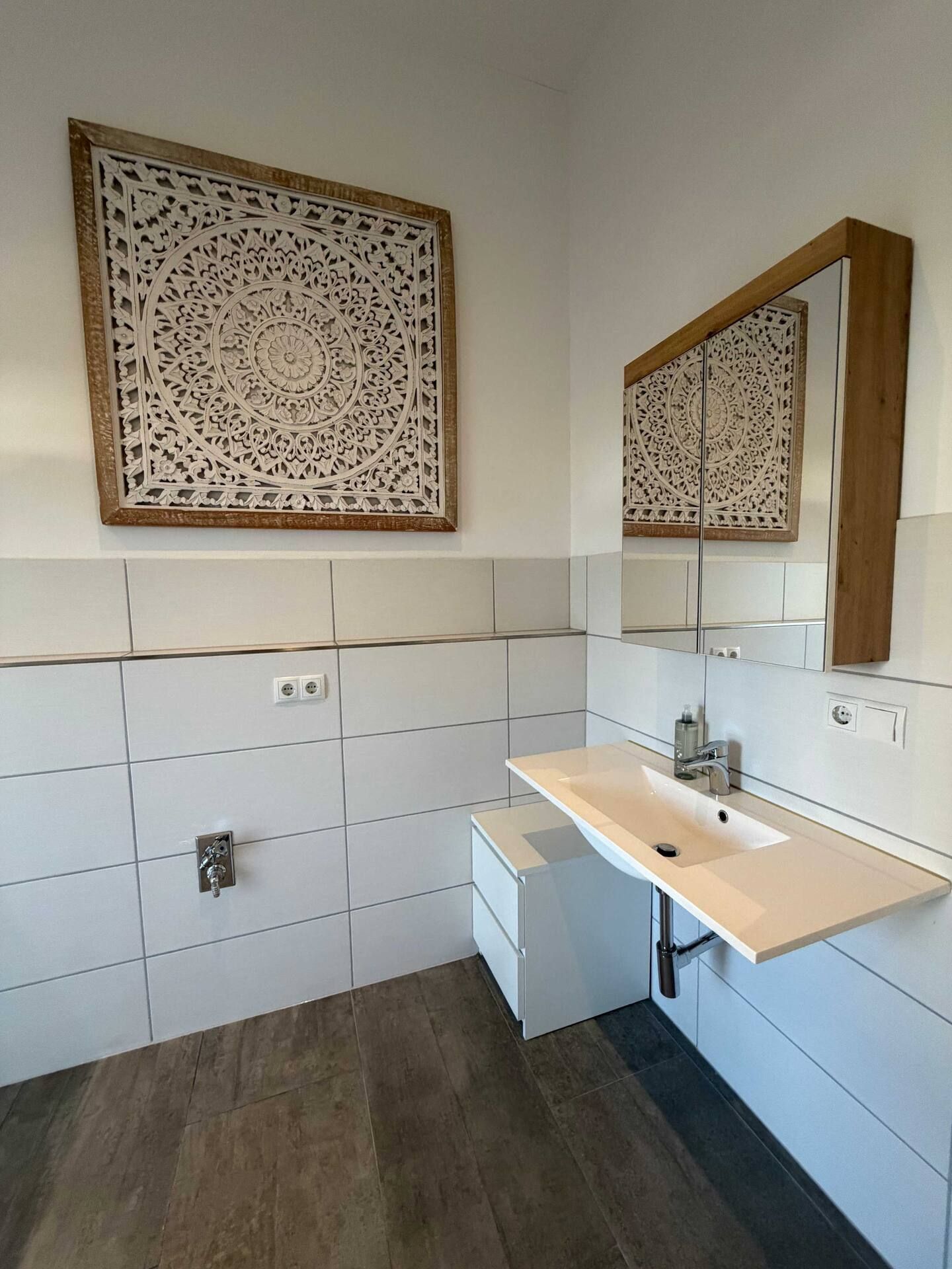 Kleines gefliestes Badezimmer mit Waschtisch aus Holz, Waschbecken, Spiegel und abstrakter Wandkunst.