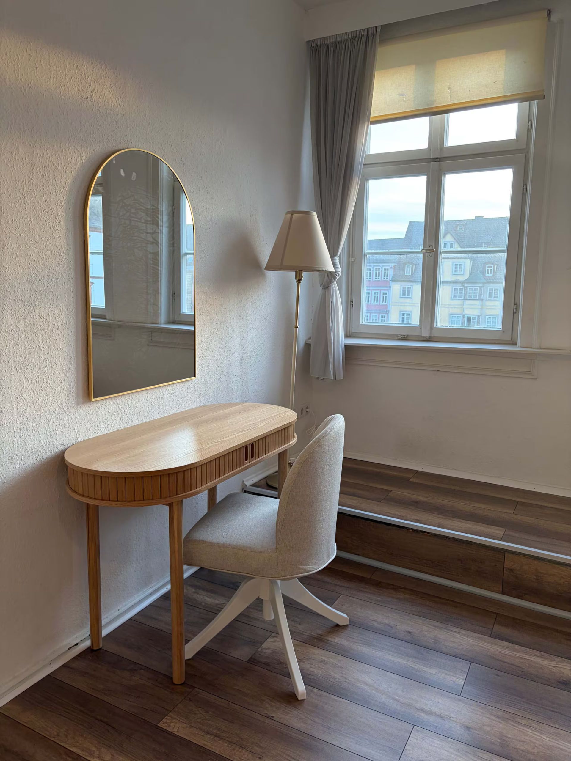 Kleiner Schminktisch und Stuhl neben einem Fenster in einem sanft beleuchteten Zimmer