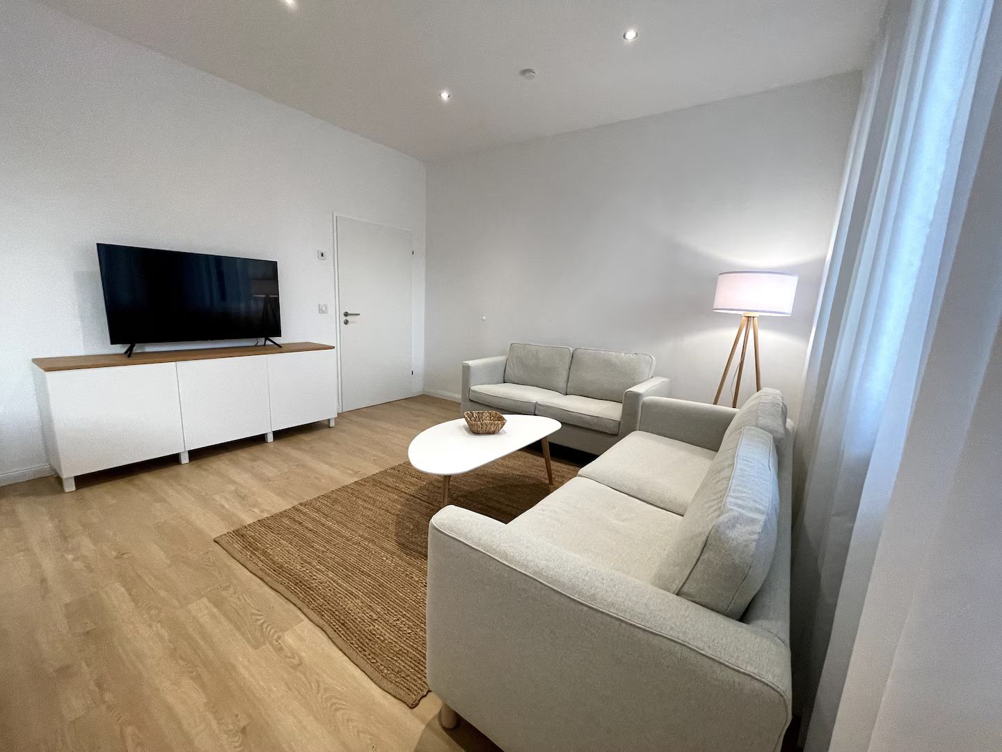 Modernes Wohnzimmer mit weißen Sofas, TV-Konsole, Stehlampe und gewebtem Teppich auf Holzboden