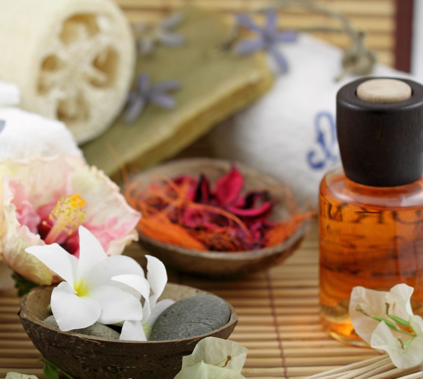 Essentiel du spa : bouteille d'huile, fleurs, savon, luffa, bol de pot-pourri, tapis en bambou.
