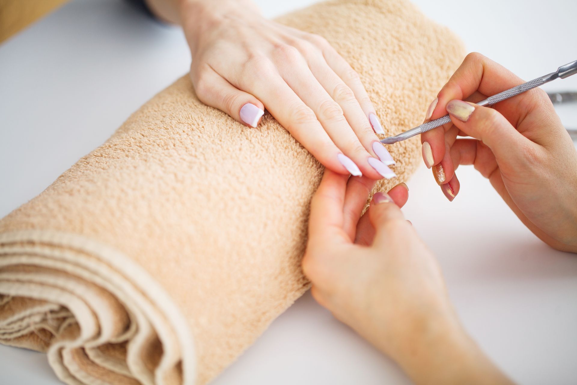 Les mains de la manucure façonnent les ongles du client avec un repousse-cuticules sur une serviette beige.