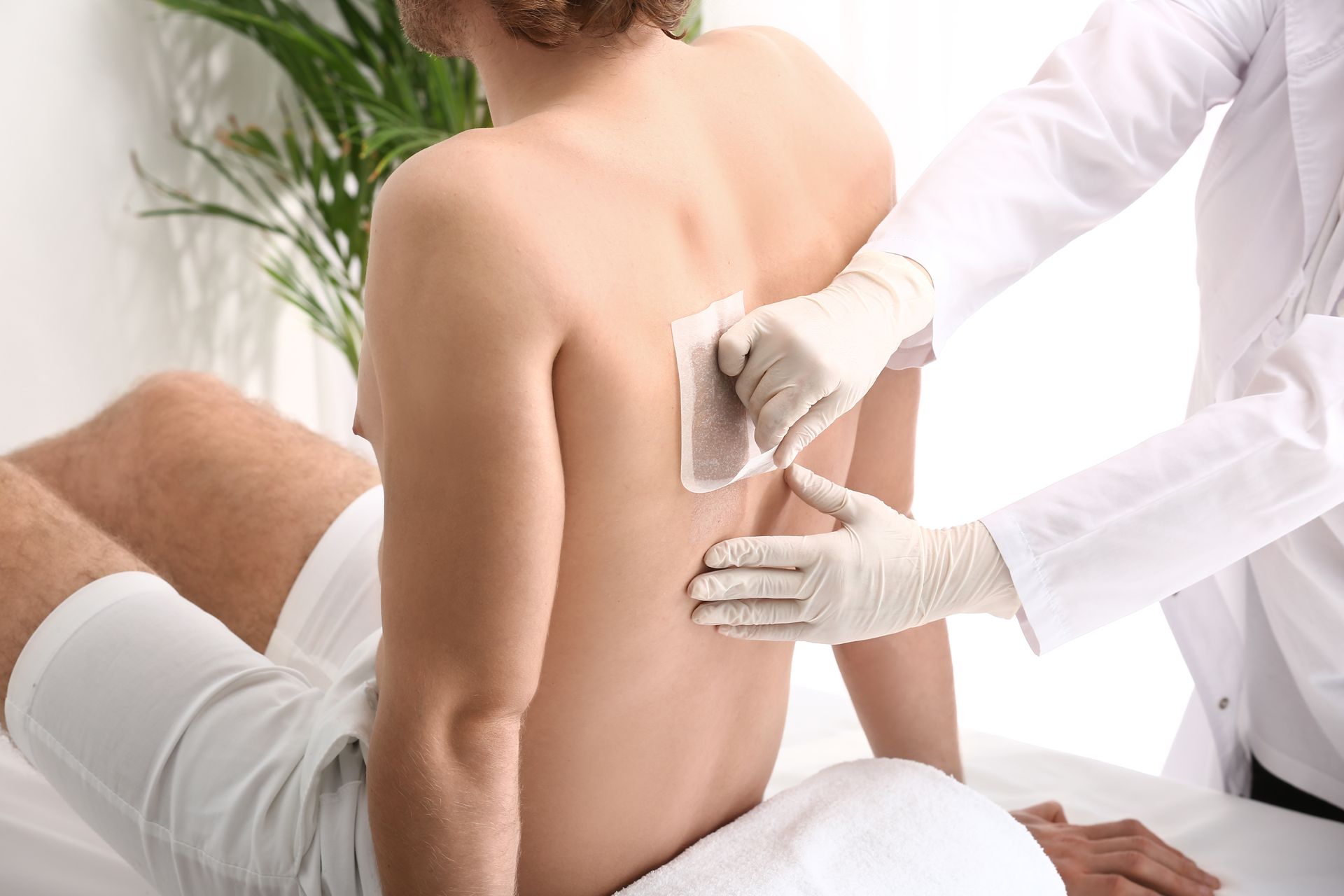 Un homme se fait épiler le dos avec une bande de cire et des mains gantées dans un salon.