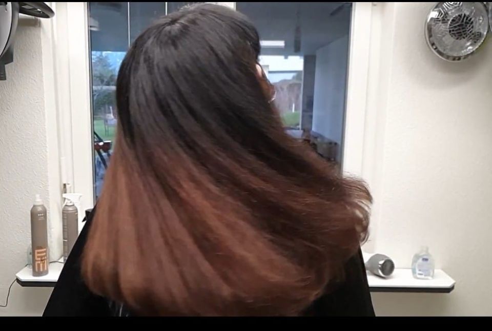 Frau mit dunklem, braun gefärbtem Haar im Ombré-Stil in einem Friseursalon. Ihr Haar weht im Wind.