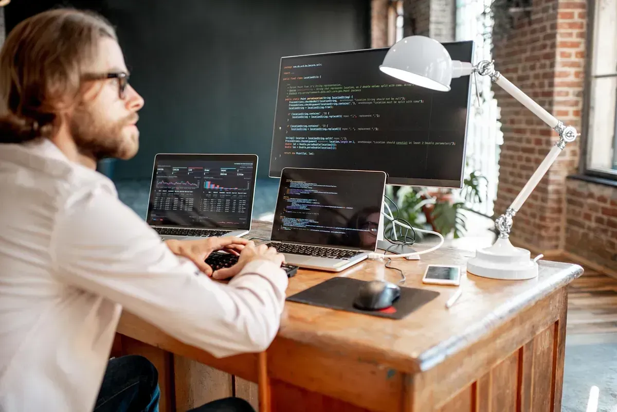 Un hombre está sentado en un escritorio con una computadora portátil y una computadora.