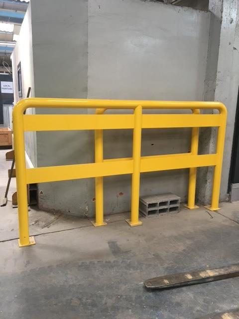 Rambarde de sécurité jaune devant un mur gris et une zone utilitaire en béton