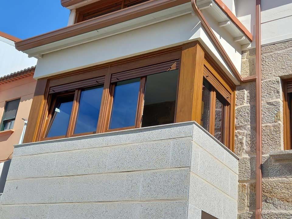Ventanas de madera marrón con persianas enrollables en un edificio de piedra bajo un techo marrón.