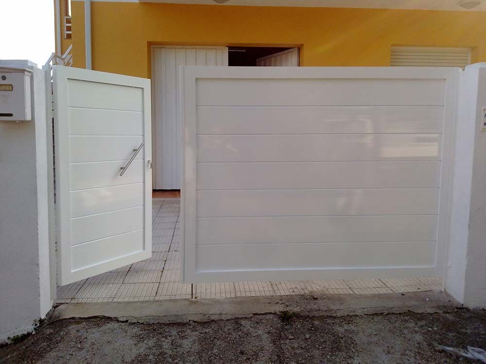 Puerta y portón blanco se abren frente a una casa amarilla con una puerta blanca.