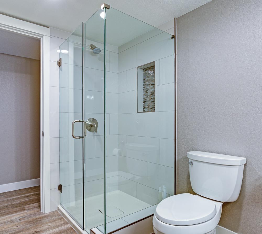 Baño con ducha de cristal, azulejos blancos, inodoro y paredes grises.