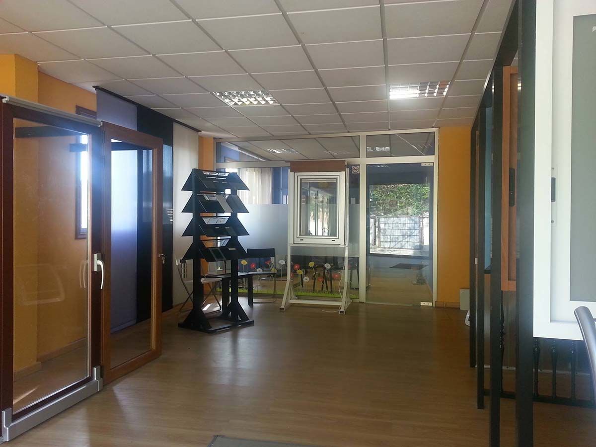 Interior de una sala de exposición de ventanas y puertas, con diversos expositores y muestras de productos.