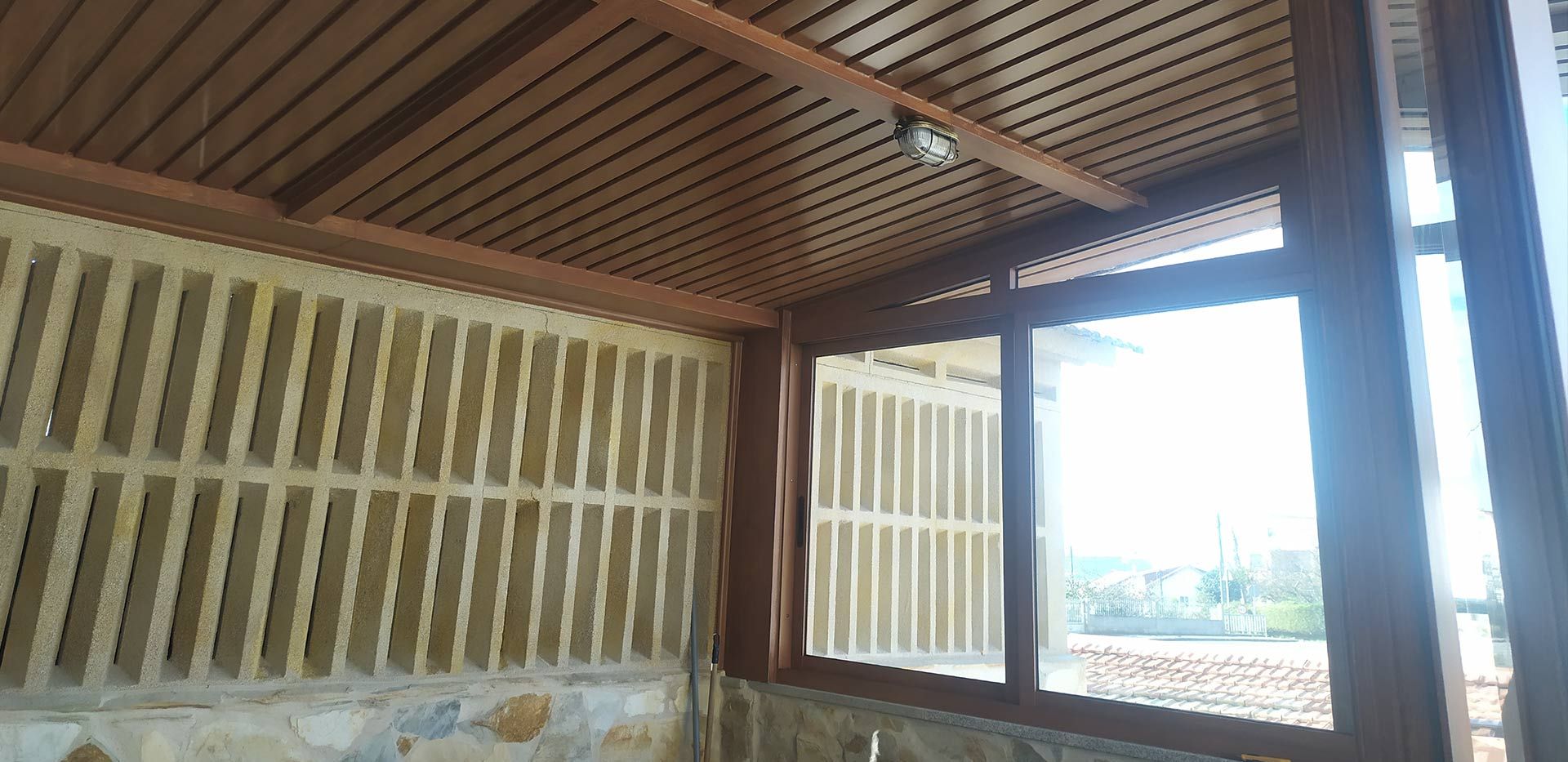 Interior de un edificio con techo, paredes y ventana de madera, con vista exterior a través de la ventana.
